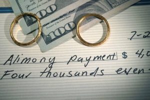 two wedding bands on top off two hundred dollar bills and a check that says alimony payment symbolizing Houston alimony and spousal support payments 